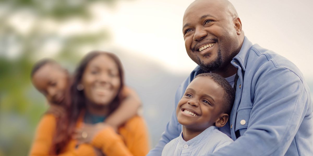 A father and mother joyfully holding their young daughter and son as they spend time together outdoors.