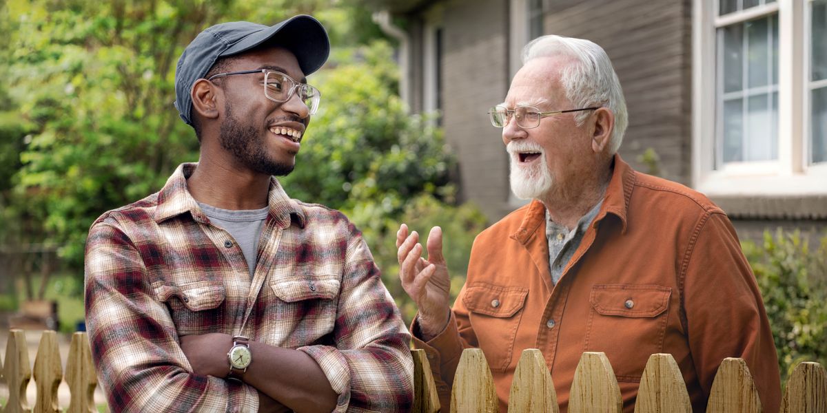 Two neighbors having a friendly conversation over a picket fence that separates their yards.