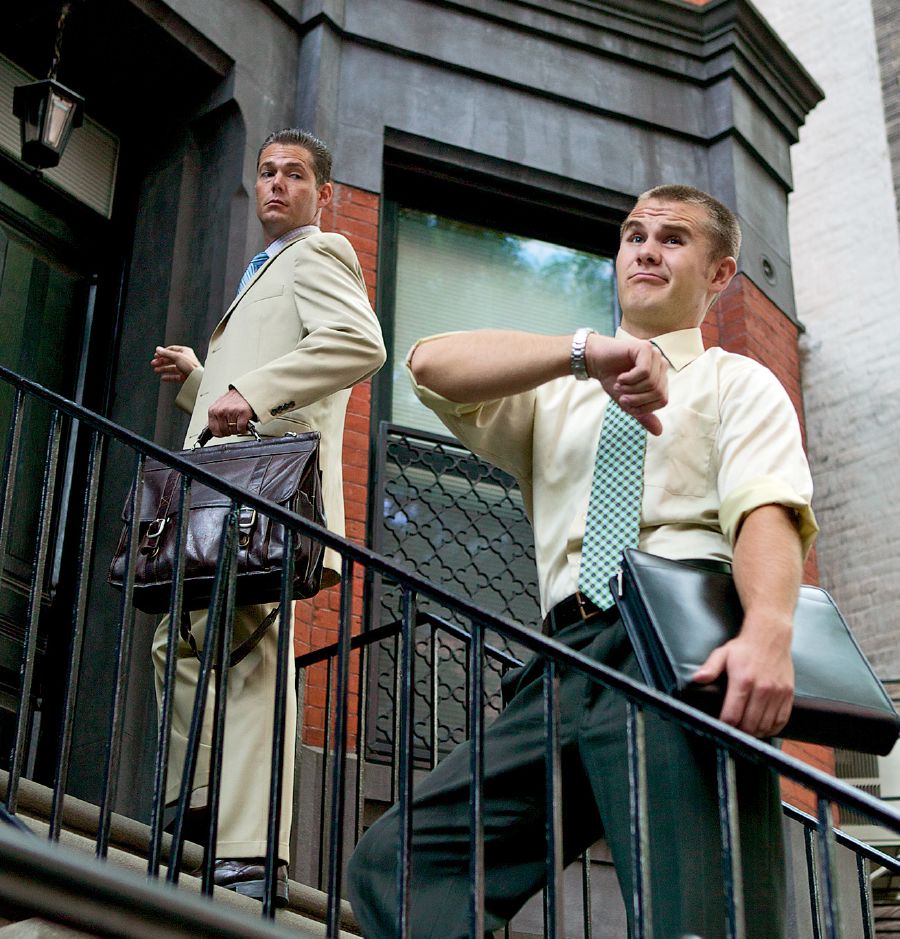 Un hermano mirando su reloj con impaciencia mientras está predicando. Su compañero lo mira de reojo.