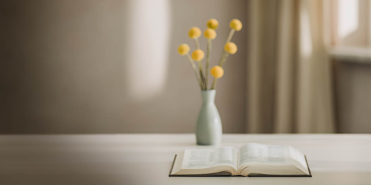 Una biblia abierta junto a un jarrón con flores.