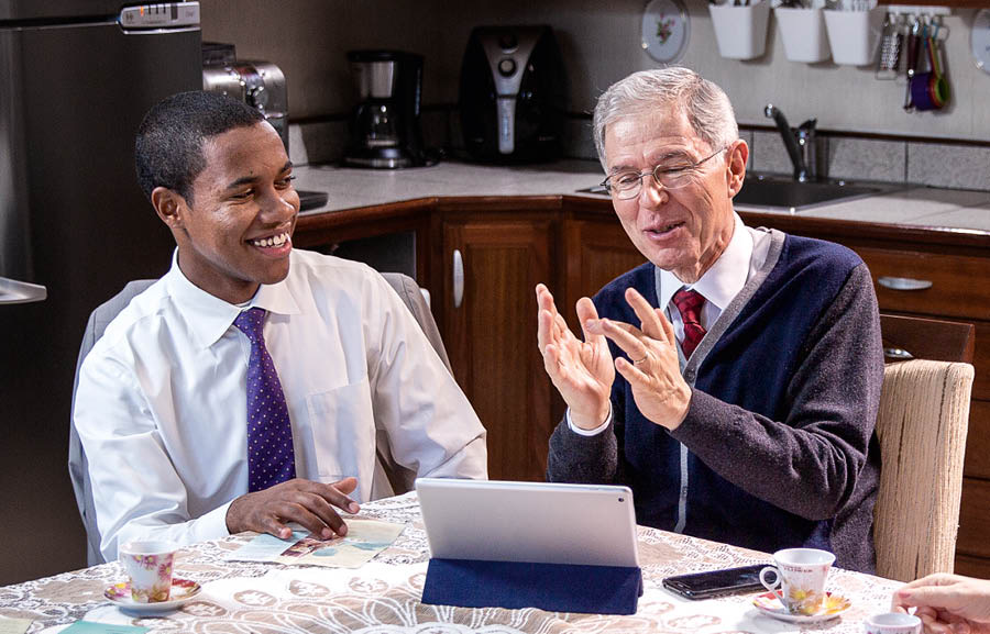 El hermano joven ayudando al hermano mayor mientras este predica por teléfono.