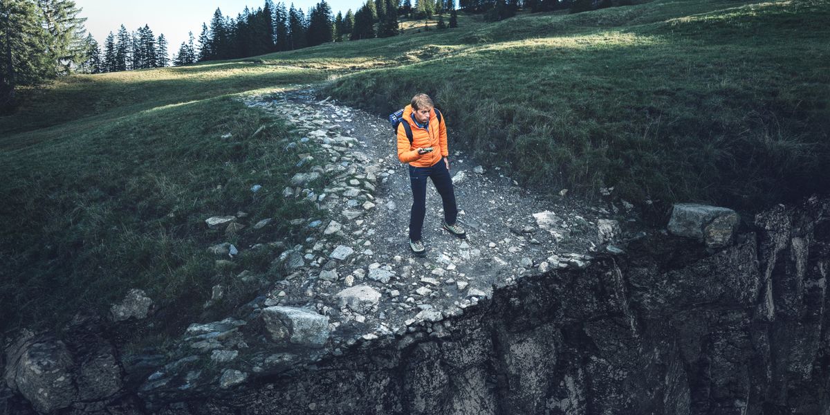 El mismo hombre joven mira su brújula mientras va por un sendero. Llega al borde de un precipicio.