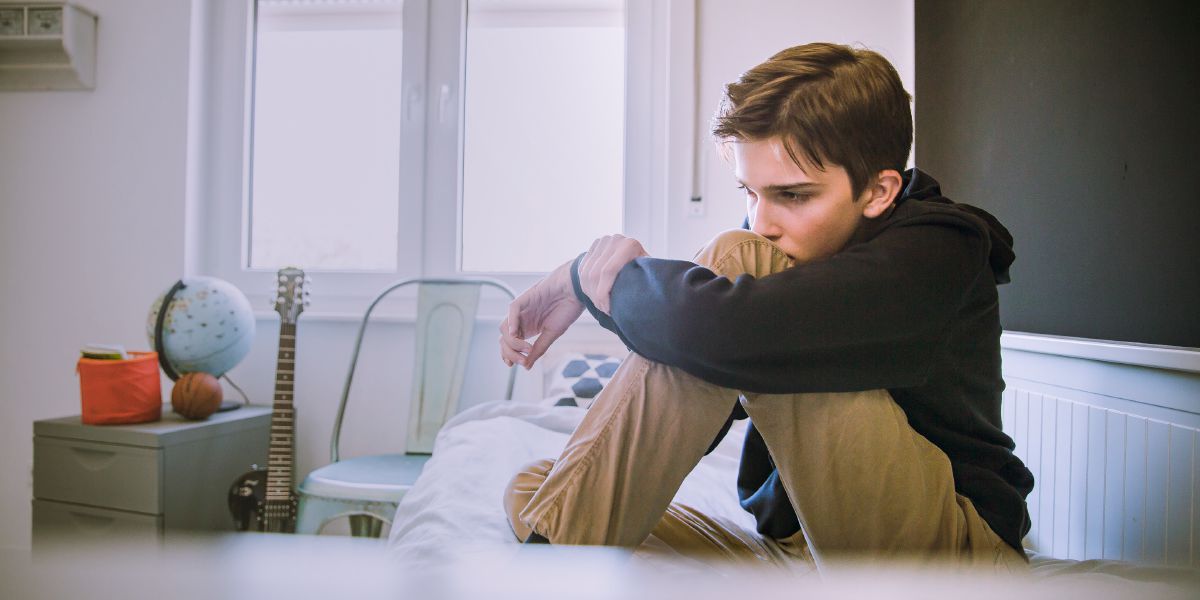 ’n Tiener sit op sy bed en lyk depressief
