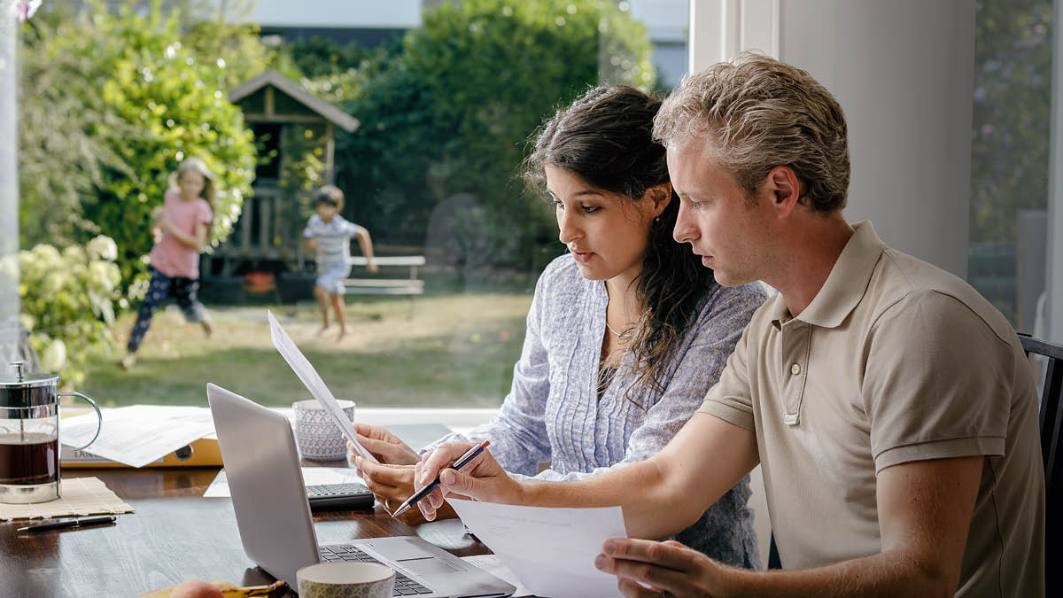 Ouers bespreek hulle finansies terwyl hulle kinders in die tuin speel.