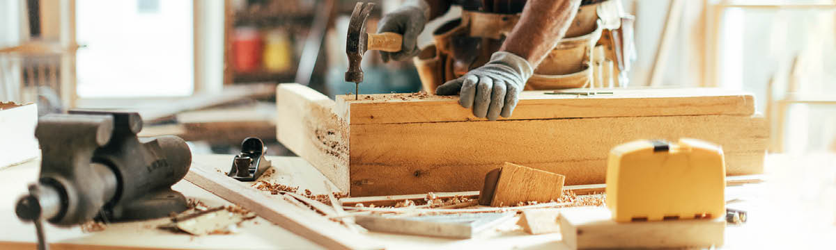 ’n Houtwerker slaan ’n spyker in ’n stuk hout.