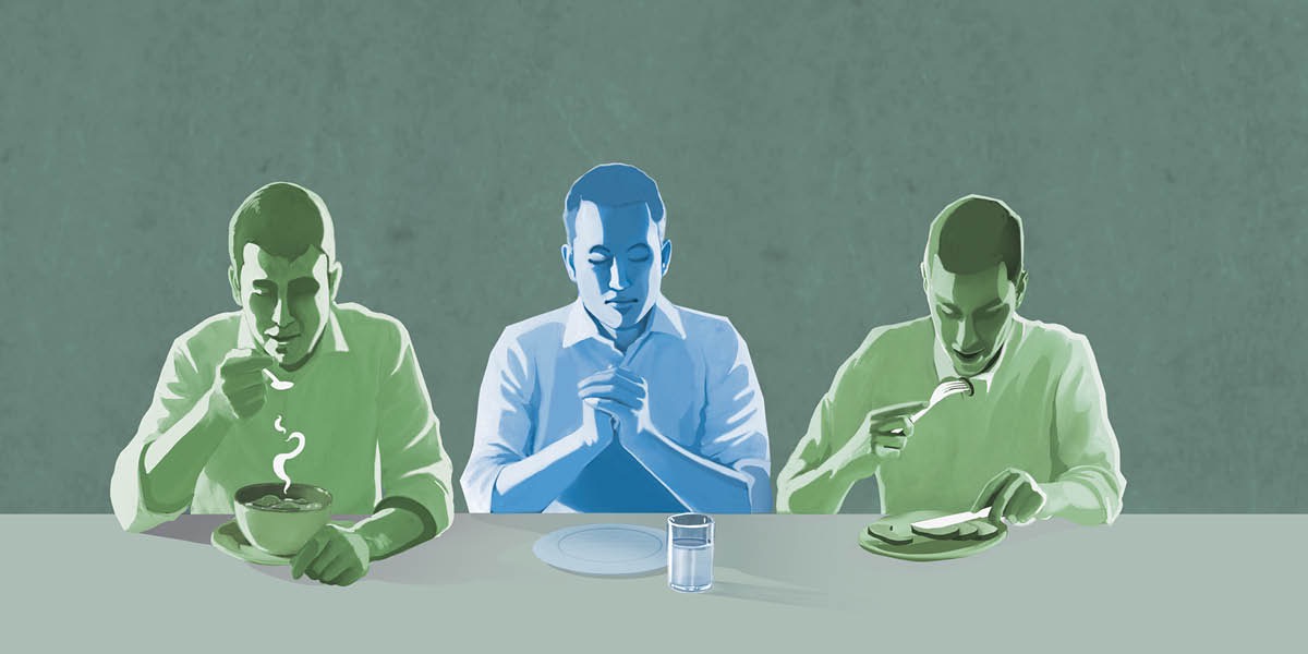 ’n Man bid met ’n leë bord voor hom terwyl mense langs hom eet