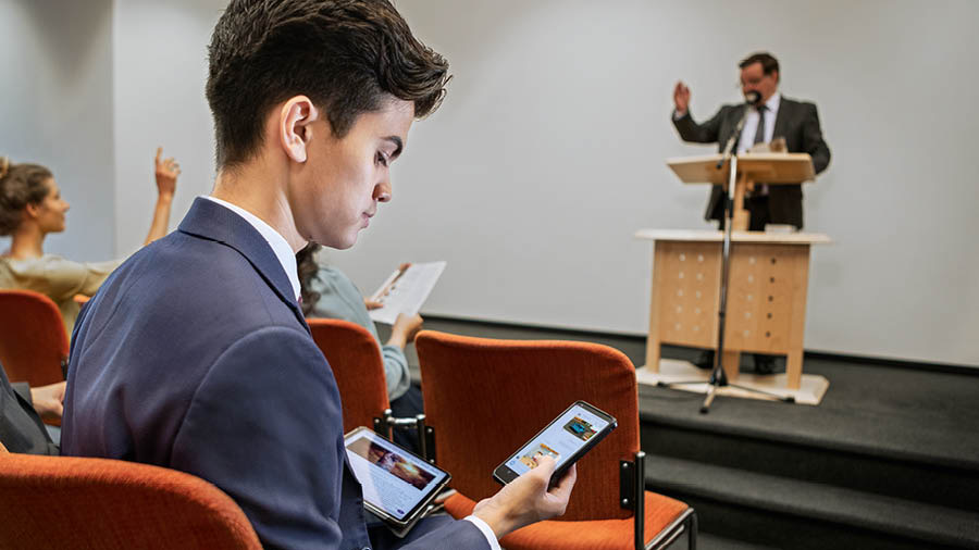 ’n Broer reageer op teksboodskappe gedurende ’n vergadering.
