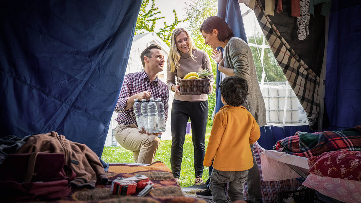 ’n Paartjie bring kos en ander voorraad vir ’n ma en haar jong seun wat tydelik in ’n tent bly.