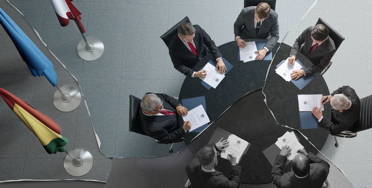’n Geskeurde foto van volksleiers wat saam om ’n tafel sit. Hulle almal teken ’n kopie van dieselfde dokument.