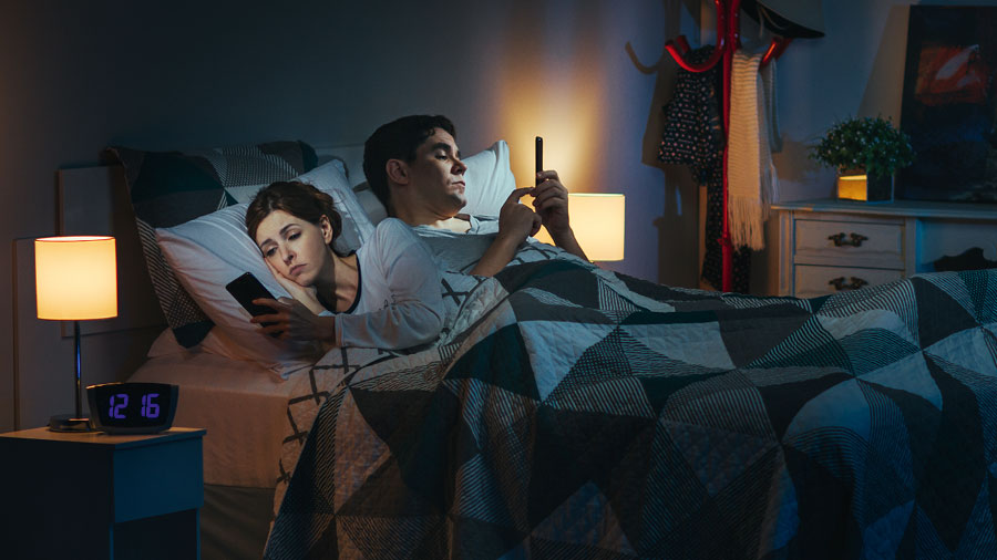زوجان يستعمل كل واحد منهما هاتفه الذكي وهو في السرير في وقت متأخر من الليل