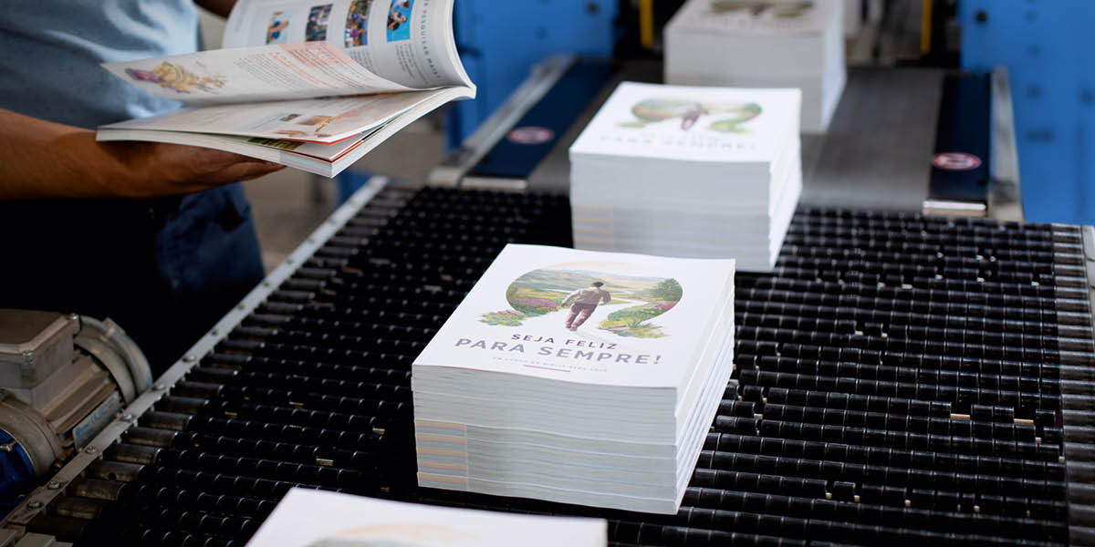 A conveyor belt transporting stacks of the “Enjoy Life Forever!” book.