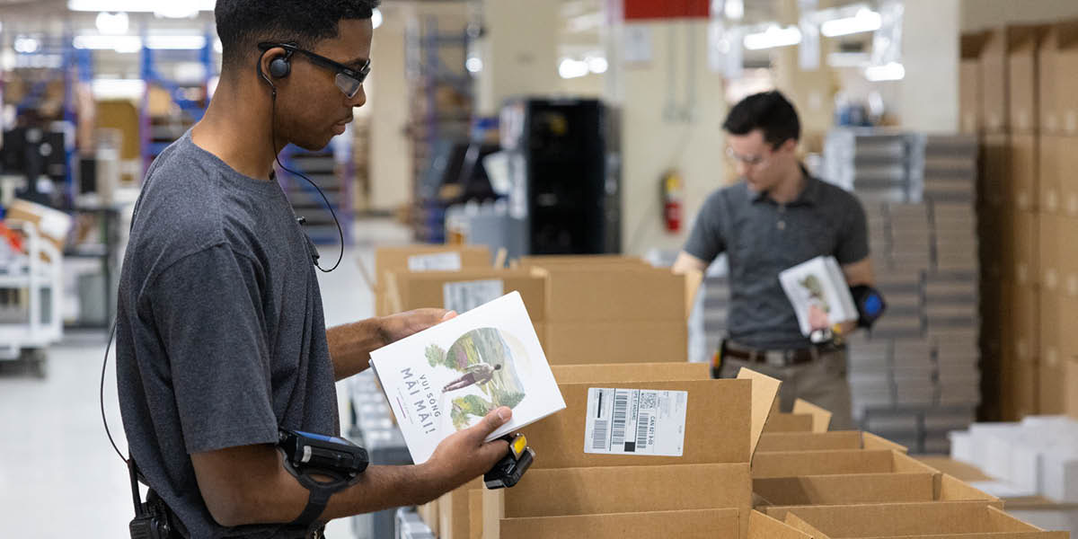 Two brothers placing books in shipping boxes.