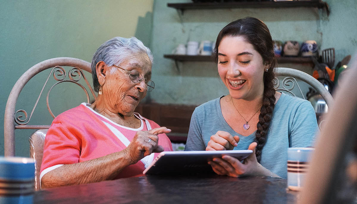 A teenage girl helping an older woman to use an electronic tablet.