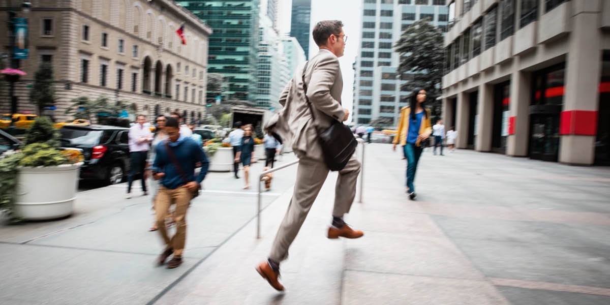 A businessman in a city running up the steps toward an office building.