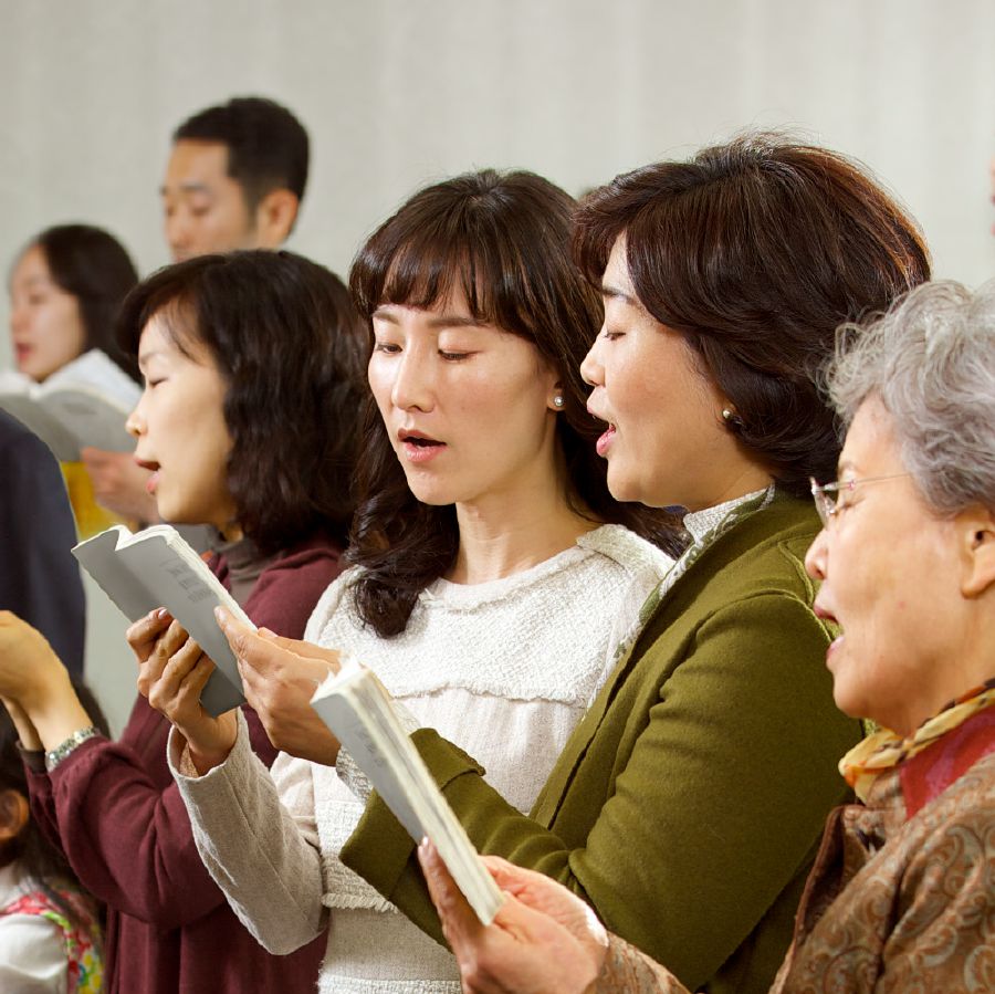 Two sisters share a songbook as they sing at a congregation meeting