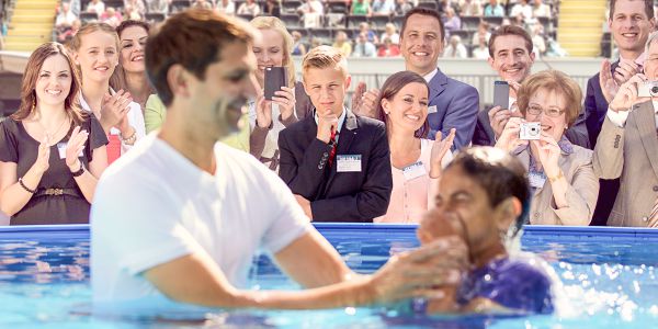 People observe a young person getting baptized, but one young man looks on with uncertainty