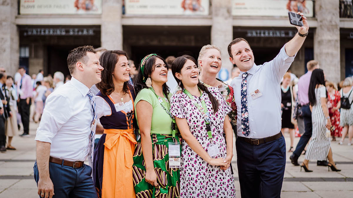 A group of happy brothers and sisters from different backgrounds, taking a selfie at a convention.