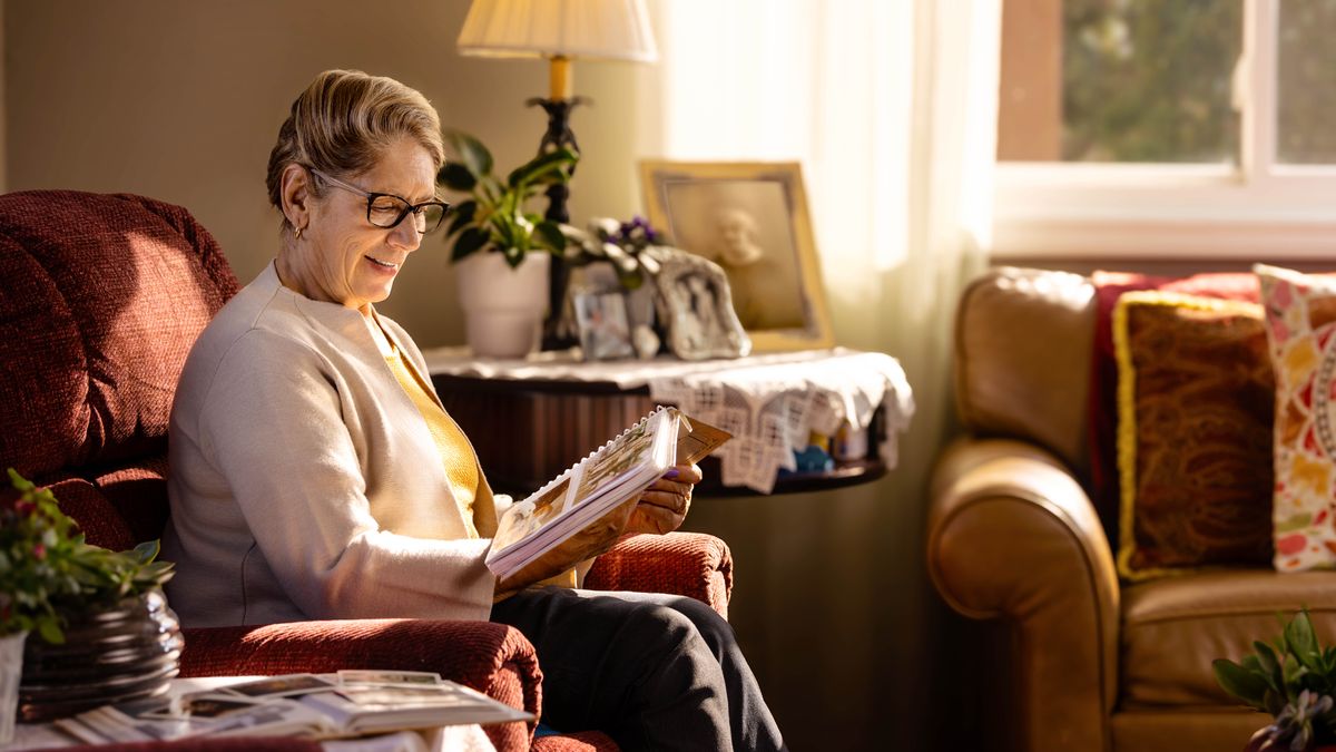 An elderly sister smiling as she looks through a photo album.