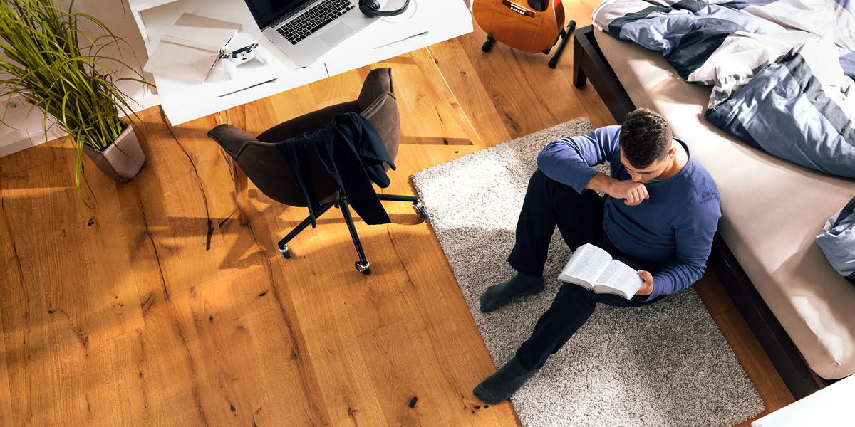 A young man sitting on the floor by his bed, reading the Bible.