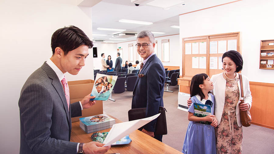 A young brother carefully checks the congregation’s literature order. An older brother observes him and smiles.