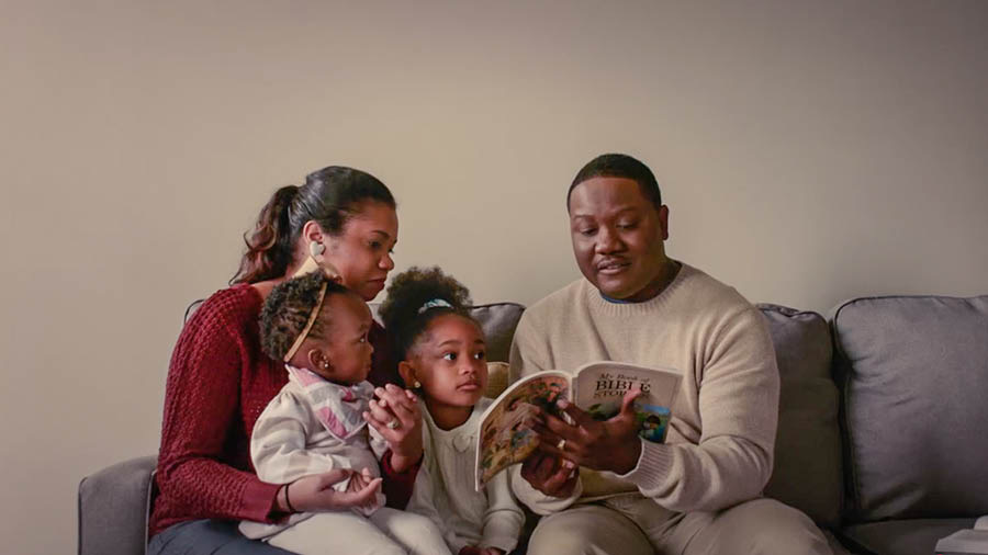 A scene from the video ‘We Must ‘Run With Endurance’​—Obey the Rules of the Contest.’ Brother Calou reading to his wife and two daughters from ‘My Book of Bible Stories.’