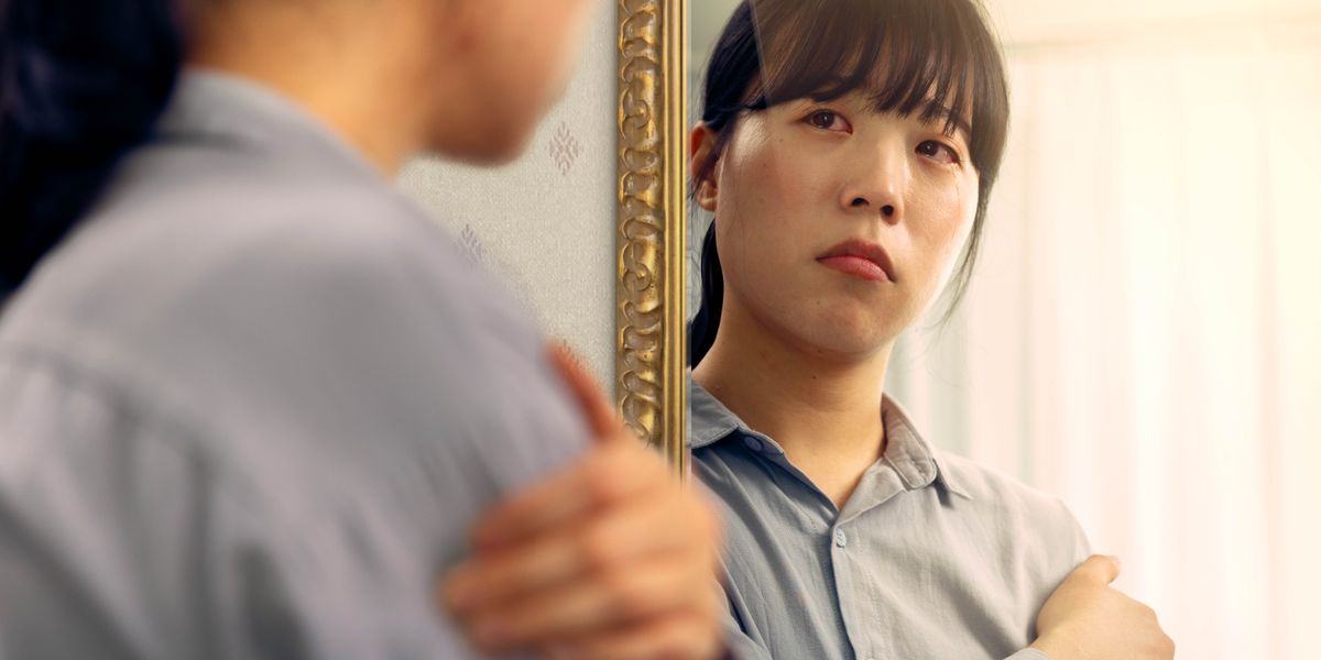 Uma mulher triste olhando para o seu reflexo no espelho.