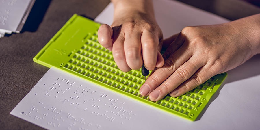 Transcrevendo um livro para o braille usando instrumentos próprios para isso.