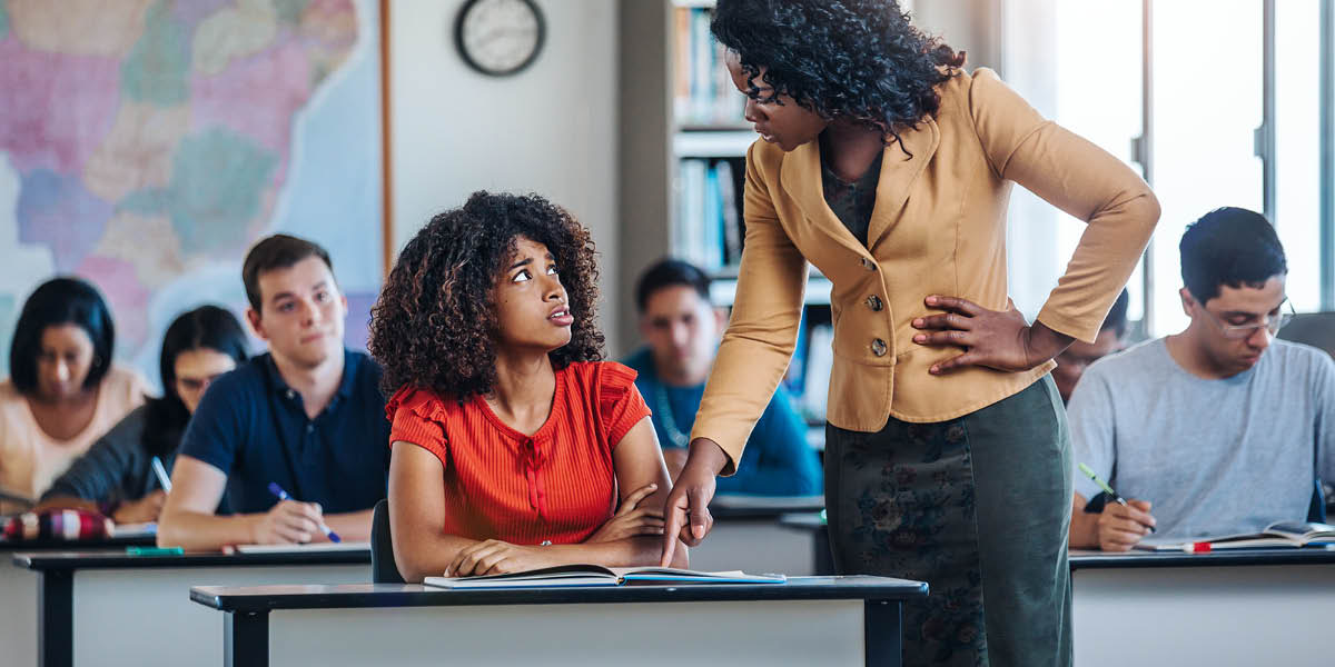 Uma professora corrigindo uma aluna na frente de toda a turma.