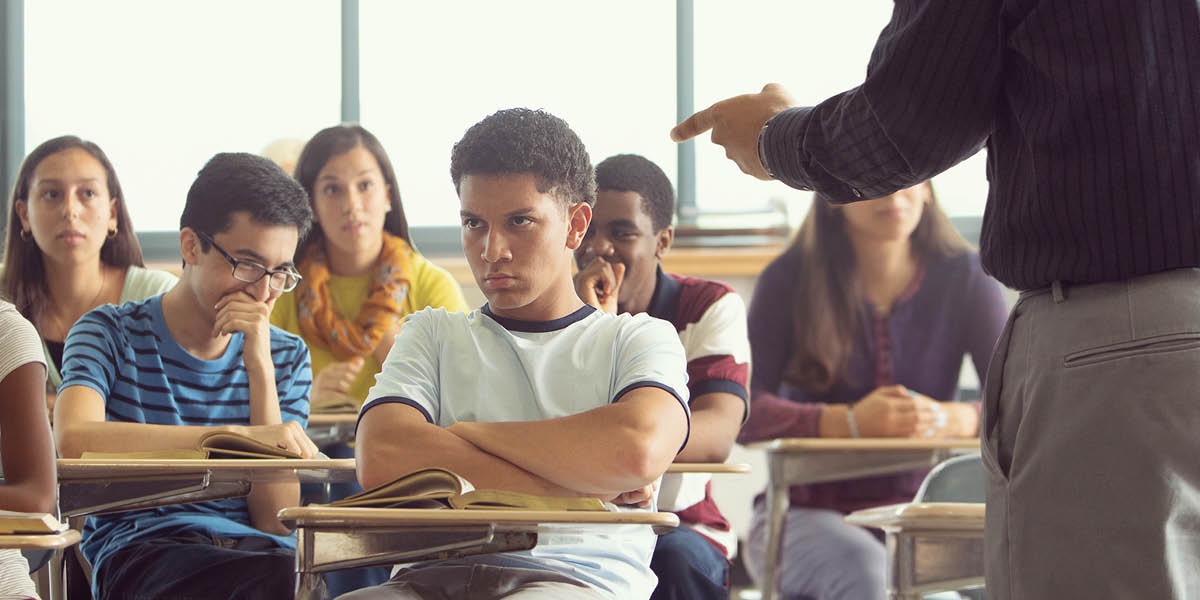 Um aluno sentado na sala de aula levando uma bronca do professor.