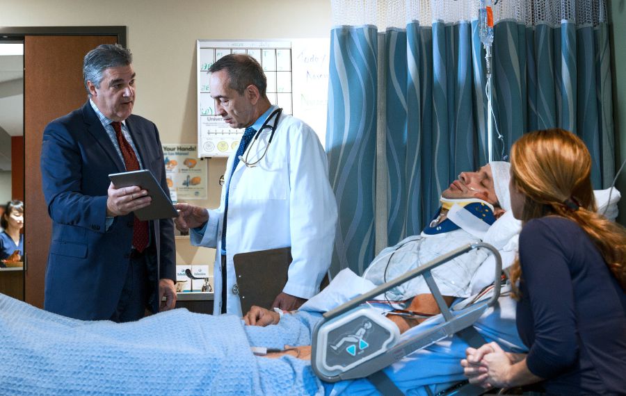 Um ancião conversando com o médico enquanto um irmão está deitado numa cama de hospital