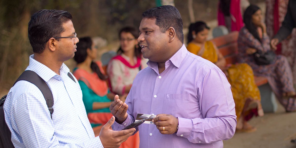 Um irmão usando um cartão de visita para mostrar o site jw.org para um homem