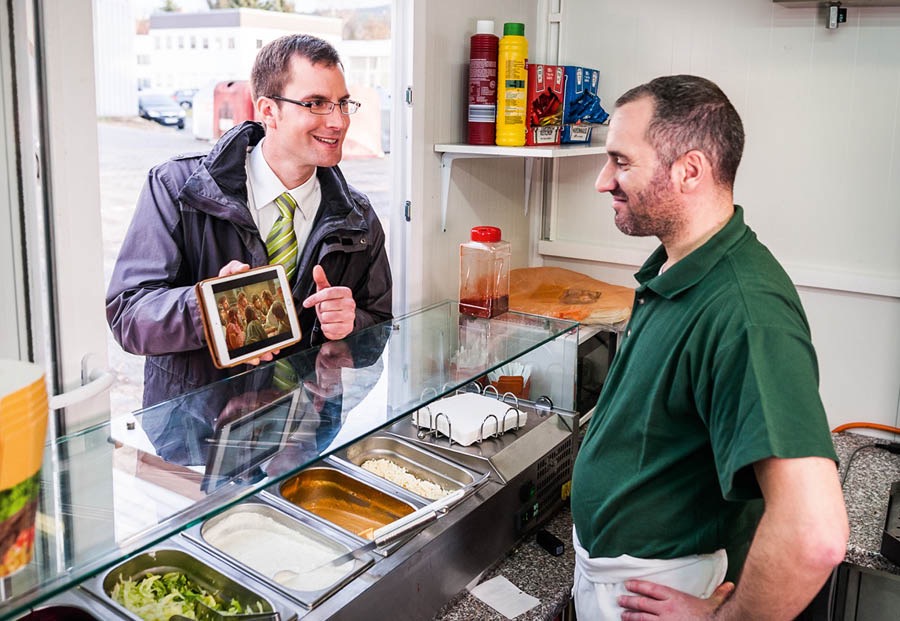 Montagem de fotos: 1. Um irmão pregando para um colega no trabalho. 2. Um irmão mostrando um vídeo num restaurante para um funcionário.