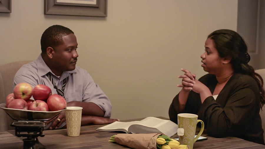  Uma cena do vídeo ‘‘Corramos com Perseverança’ — Obedeça às Regras da Competição’. O casal Santos conversando com calma sobre seus problemas. Uma Bíblia está aberta na frente deles.