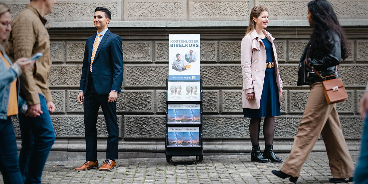 Un matrimoni content al costat d’un exhibidor de publicacions amb un cartell que anuncia els nostres cursos bíblics gratuïts.