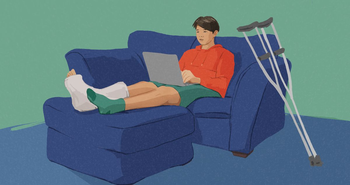 Batan-ong lalaki nga nabalian ug gisemento ang tiil naglingkod sa sofa samtang nag-laptop.