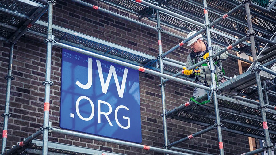 Svědek Jehovův montuje lešení na budově určené k uctívání Jehovy