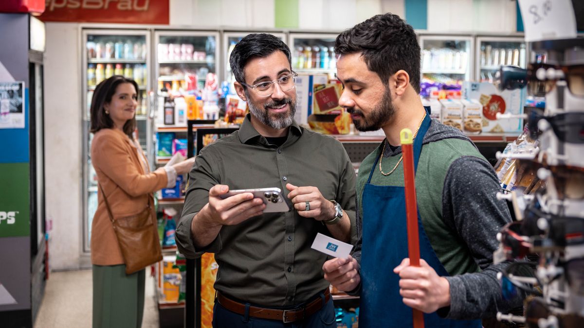 Později je ten bratr v obchodě s potravinami, jednomu zaměstnanci podal vizitku jw.org a ukazuje mu něco na svém telefonu. Jeho žena stojí opodál a s úsměvem je pozoruje.