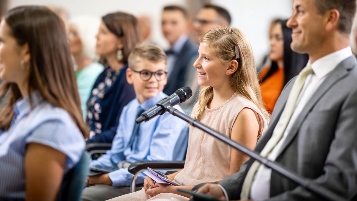 Ta sestra dává komentář na shromáždění a její bráška se na ni s úsměvem dívá.