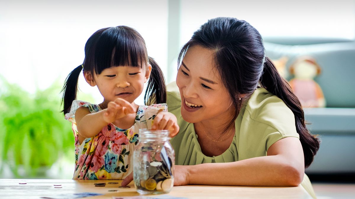 Una niña echa moneditas en un bote mientras su mamá la mira contenta.