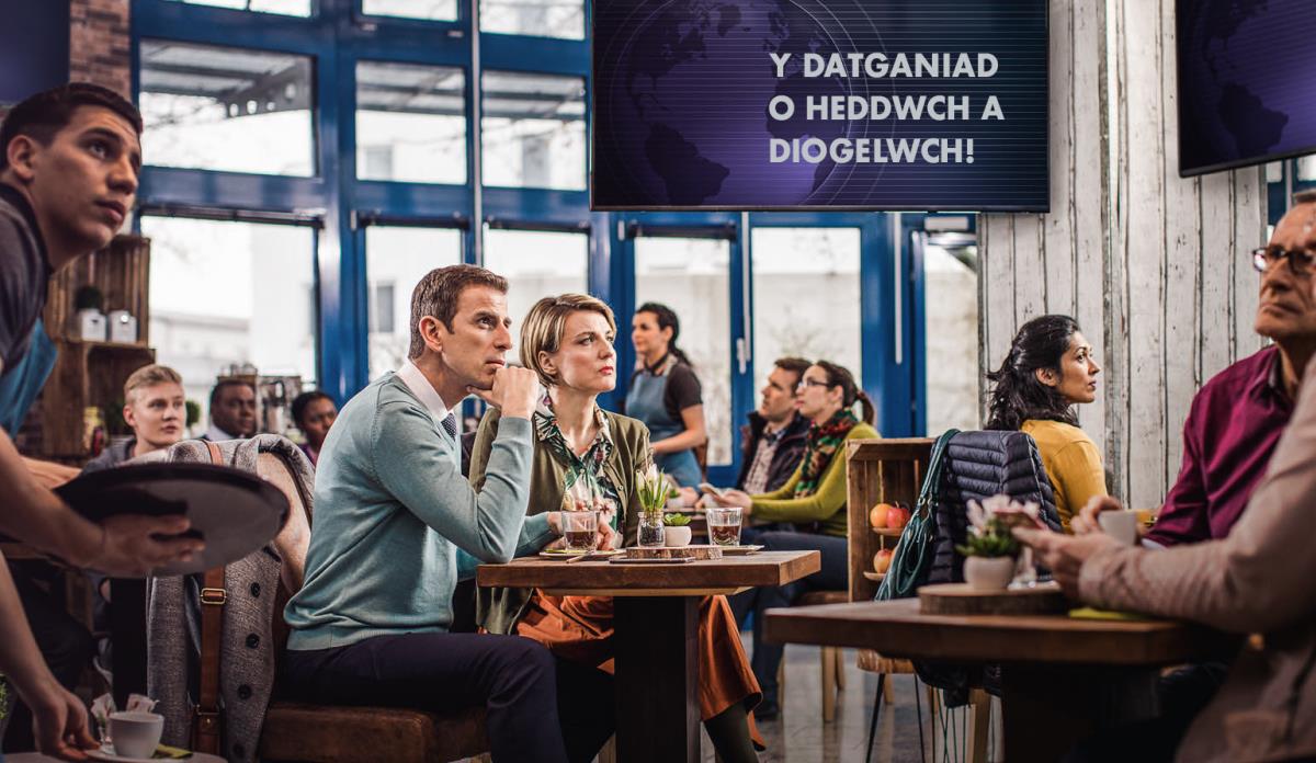 Cwsmeriaid mewn siop goffi wedi eu synnu ar ôl clywed neges ar y newyddion yn datgan “heddwch a diogelwch,” ond nid yw’r cwpl sy’n Dystion yn cael eu twyllo