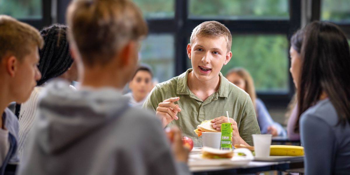 En teenagedreng taler med nogle klassekammerater mens de spiser i frikvarteret.