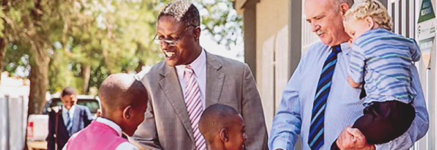 Johny und Gideon begrüßen vor einem Königreichssaal von Jehovas Zeugen einige Kinder.