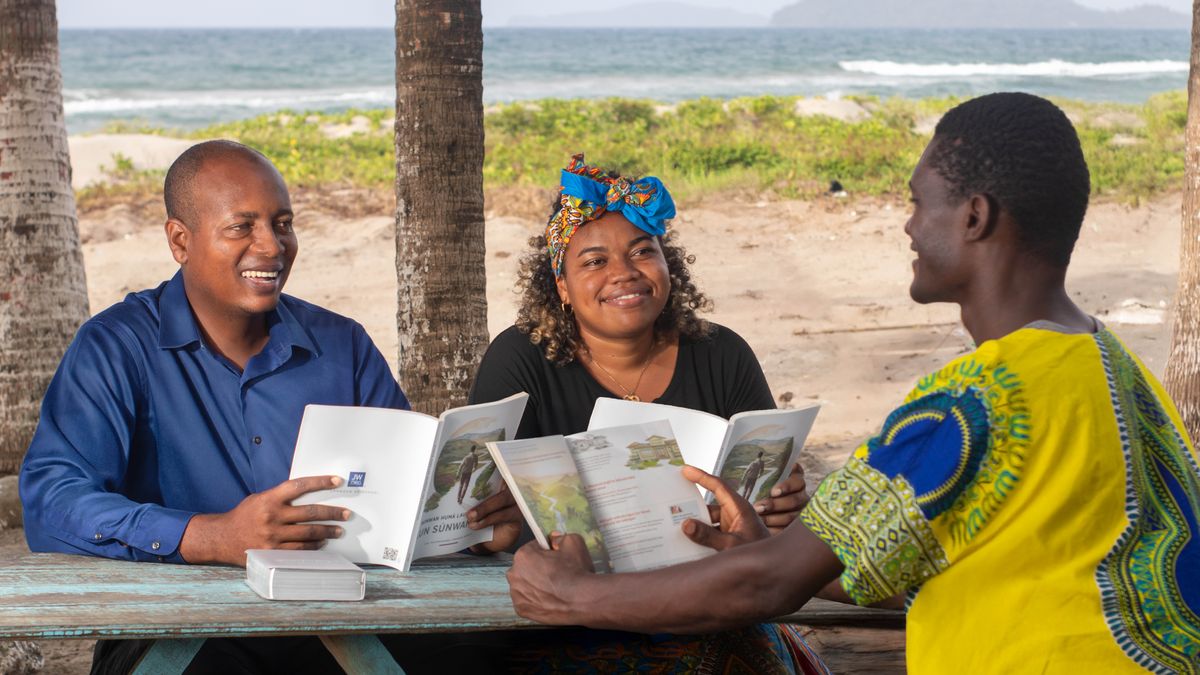 In der Nähe eines Strandes studiert ein Ehepaar mit einem Mann das Buch „Glücklich – für immer“.