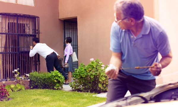 Zwei Zeugen Jehovas im Haus-zu-Haus-Dienst werden von einem Mann dabei beobachtet, wie sie durch ein Fenster spähen