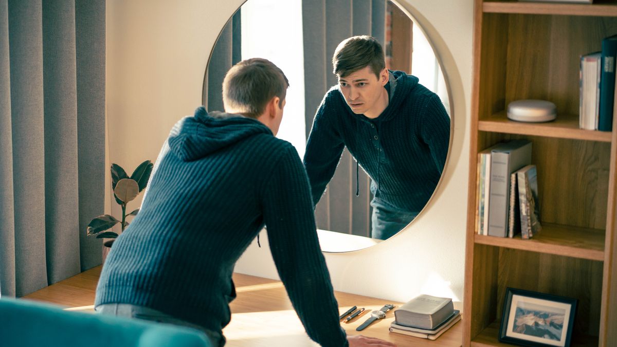 Der junge Bruder denkt über seine Schwäche nach und schaut dabei traurig in einen Spiegel.