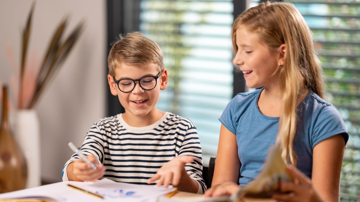 Ein Mädchen liest ihrem kleinen Bruder eine biblische Geschichte aus einem Buch vor und er malt dazu ein Bild.