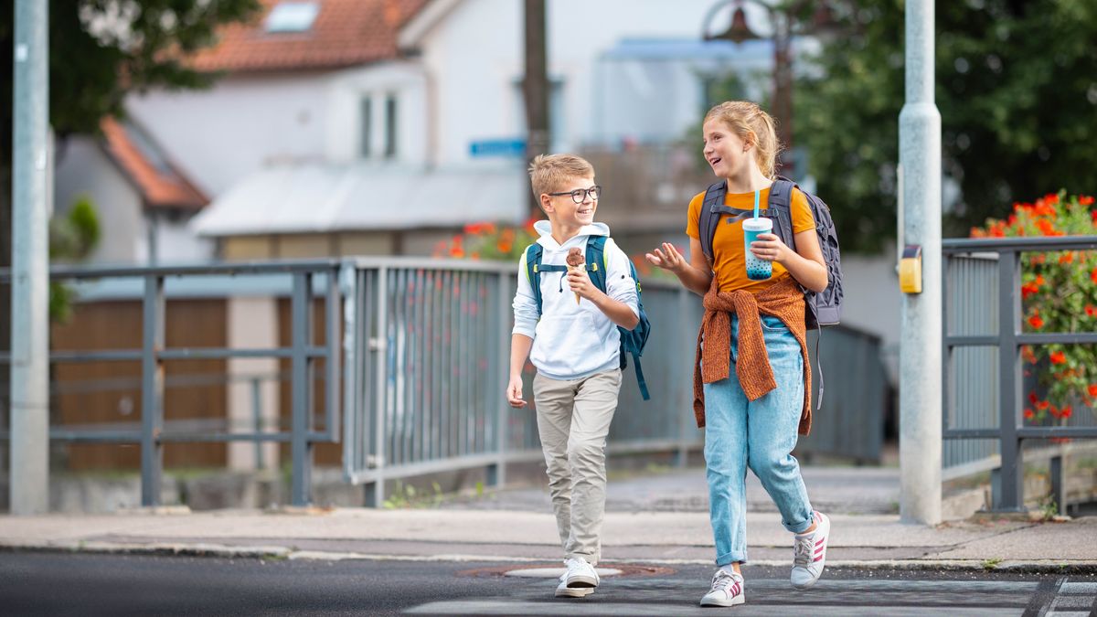 Das Mädchen und ihr Bruder unterhalten sich gutgelaunt auf dem Schulweg und genießen dabei eine Erfrischung.