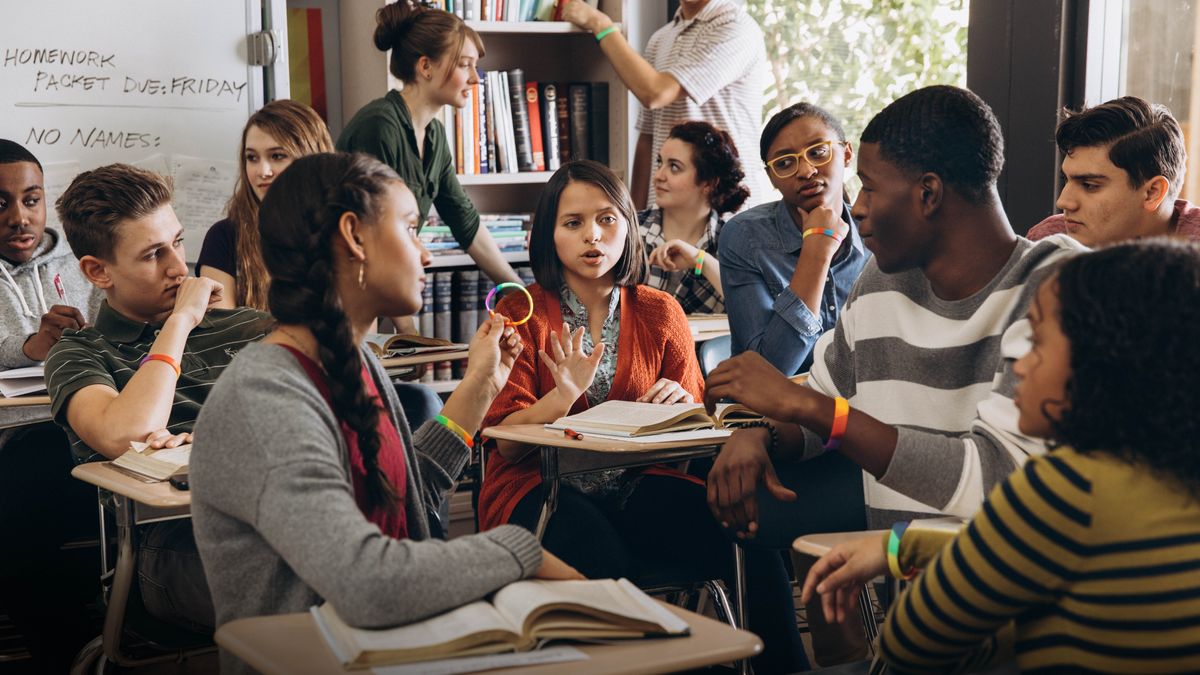 Später im Klassenzimmer: Ihre Mitschüler drängen die Schwester, ein Regenbogen-Armband zu tragen. Sie sehen sie ungläubig an, weil sie höflich ablehnt.