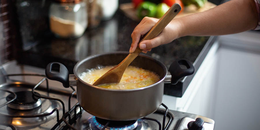 Una mujer calienta sopa en una olla.