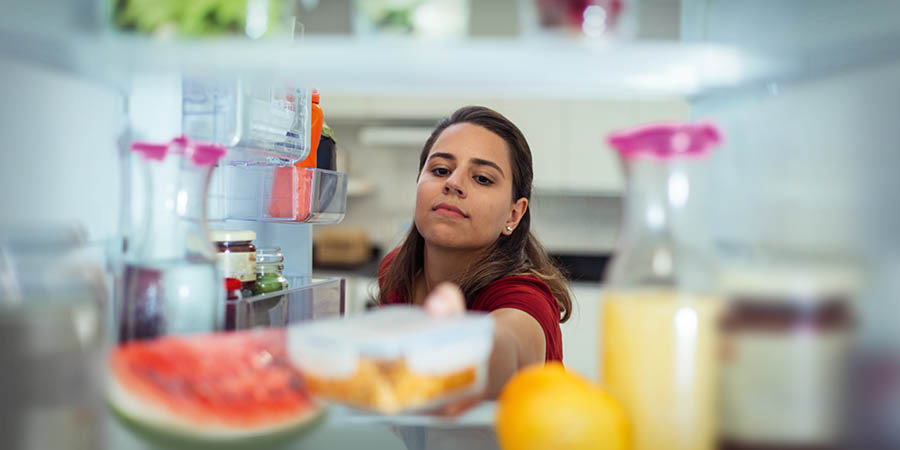 Una mujer guarda un recipiente cerrado con comida en el refrigerador.